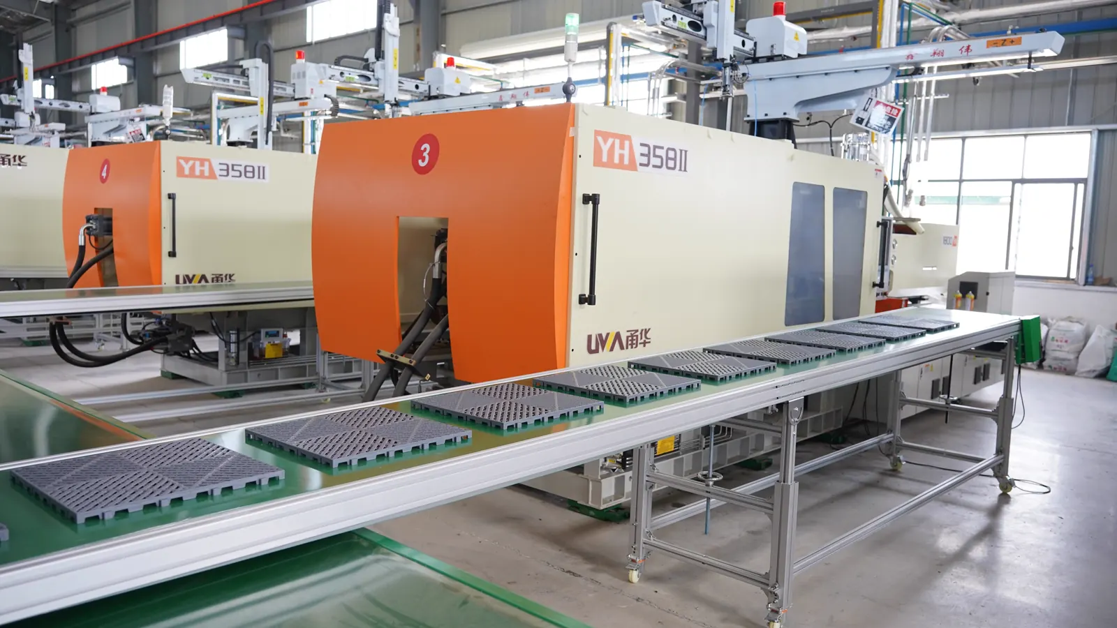 Modular floor tiles on a conveyor beside injection-molding equipment